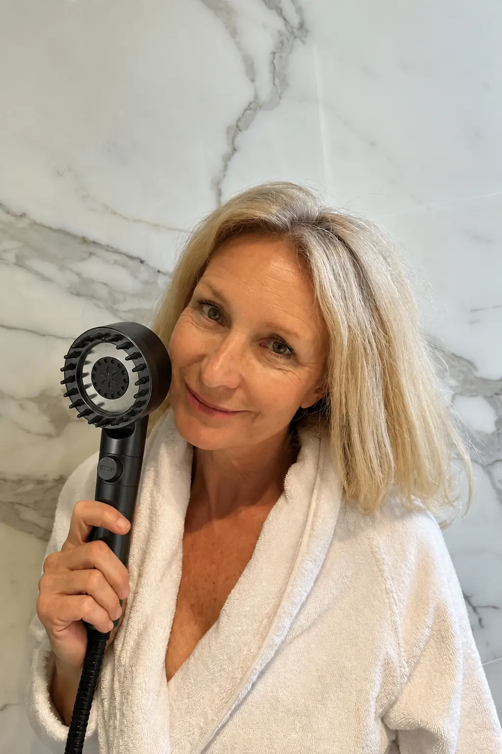 Customer holding a black RAINLY shower head in a marble bathroom