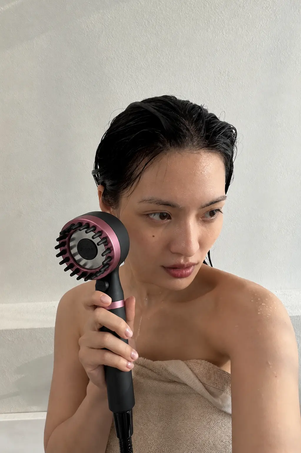 Customer with wet hair holding a black and pink RAINLY shower head