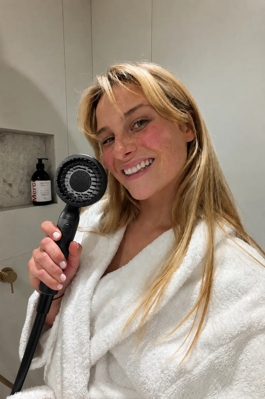 Smiling customer in a robe holding a black RAINLY shower head